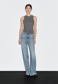 Grå ärmlös topp med rund halsringning, kombinerad med ljusblå vida jeans. Jeansen har en urblekt look och en klassisk femficksdesign.