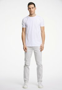White cotton t-shirt paired with light gray trousers and white sneakers. The t-shirt features short sleeves and a round neckline.