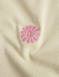 Beige ribbet stof præsenterer et pink broderet blomsterdesign i midten, der fremh�æver klare kronblade og en rund midte.