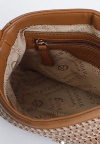 Interno di una borsa a tracolla marrone con una tasca con zip e fodera beige impresso con un motivo di logo ripetuto.