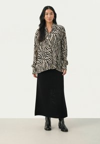 Dyreprint button-up skjorte i beige og sort, parret med en sort ribbet maxiskirt og sorte ankelstøvler. Lange ærmer med manchetter.