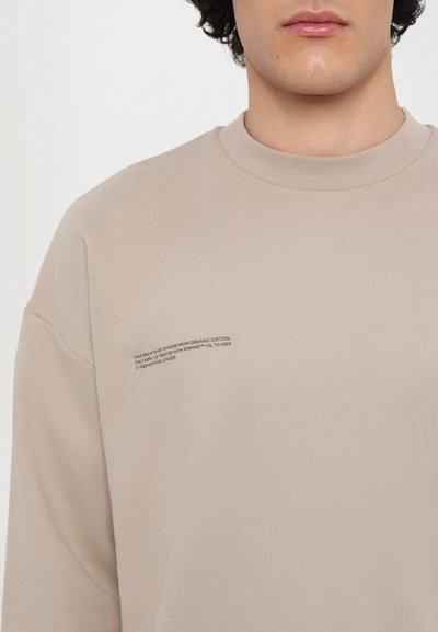 Beige sweatshirt made from organic cotton with a crew neckline. Features printed text on the left side detailing fabric treatment.