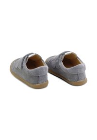 Zapatos de ante gris con una textura suave, cuentan con una correa de velcro y una suela de goma texturizada. El diseño incluye acentos de costura sutiles.