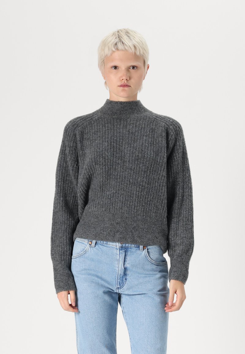 Gray, ribbed knit sweater with a high neck, dropped shoulders, and long sleeves. Paired with light blue denim jeans.