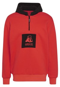 Felpa rossa con cappuccio nero. Presenta un collo a mezza zip e una toppa quadrata nera sul petto con un logo orso e la scritta "adidas ADVENTURE".
