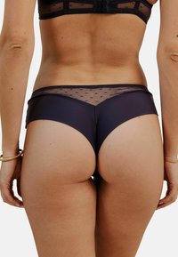 Culotte noire avec un dos en maille transparente ornée de motifs à pois, conçue en taille basse et fabriquée dans un tissu lisse et extensible.