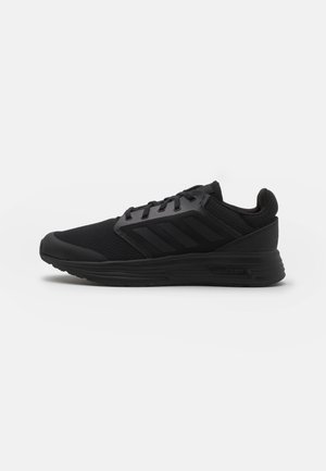 Czarny sportowy sneaker z teksturą siateczkową na cholewce, zawiązywany na sznurowadła, z amortyzowaną podeszwą i subtelnym wzorem trzech pasków z boku, przedstawiony z profilu.