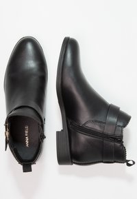 Black leather ankle boots with a rounded toe, side zipper, and strap detail. Smooth texture with a low stacked heel.