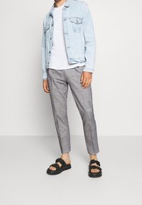 Light blue denim jacket over a white shirt, paired with gray checkered trousers and black sandals featuring a buckle detail.