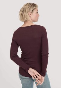 Bordeaux langarm overhemd van rekbare stof, slim fit ontwerp met een ronde halslijn, minimale naden, gedragen met lichtblauwe jeans.
