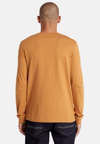 Langsleeve shirt in mosterdkleur, gemaakt van zachte katoen, met een ronde halslijn en een eenvoudig ontwerp, met een rechte snit en minimale naden.