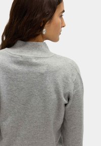 Grijze trui met een hoge hals, eenvoudig ontwerp en zachte textuur. Heeft een geribde kraag en naadloze schouders. Korte mouwen zichtbaar.