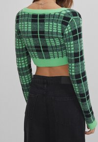 Zielony i czarny kraciasty krótki sweter z długimi rękawami, wykonany z miękkiego, puszystego materiału. Charakteryzuje się szerokim dekoltem i dopasowaną talią.