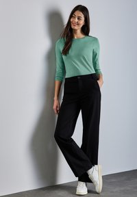 Mint-vihreä pitkähihaisten paita yhdistettynä korkeavyötäröisiin mustiin housuihin. Asua täydentävät valkoiset lenkkarit ja minimalistinen muotoilu.