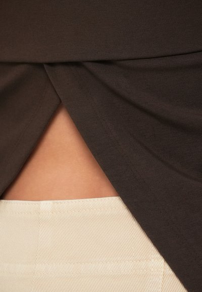 Σκούρο καφέ τοπ με λεπτομέρεια υφάσματος που πέφτει, αποκαλύπτοντας μια ανοιχτό κρεμ, ριμπ υφή φούστα από κάτω. Απαλά, ελαφριά υλικά.