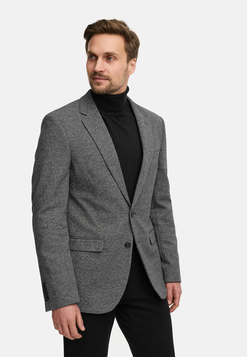 Szürke textúrájú zakó, elegáns nyakkivágással, két elülső zsebbel és egy gombos záródással, fekete garbóval párosítva.
