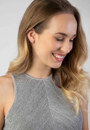 Zilverkleurige jurk met een hoge halslijn, met een visgraatpatroon. Een model draagt delicate ringoorbellen en heeft golvend haar.