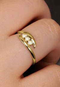 Goldring mit einem gewölbten Design, das klauenartige Akzente und drei eingearbeitete klare Kristalle aufweist, auf einem Finger präsentiert.
