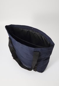 Marineblauwe tote bag met zwarte stoffen riemen. Beschikt over een ruime binnenkant met een gladde textuur en een binnenvak. Drukknoopsluiting aan de bovenkant.
