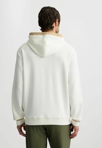 Weißer Hoodie mit einem sandfarbenen Kragen, ausgestattet mit einer Kordelzugkapuze, lockerer Passform und gerippten Bündchen. Texturiertes Material mit glatter Oberfläche.