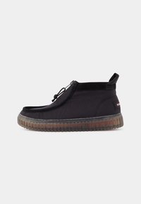Chaussure noire à enfiler avec semelle claire côtelée, fermeture éclair, languette de tirage au talon et petite étiquette logo sur le côté arrière.