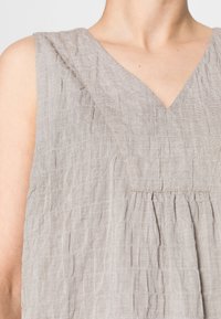 Bezramienna szara tunika z dekoltem w serek, z pomarszczoną strukturą i subtelnymi detalami szycia wzdłuż dekoltu i fałd.