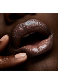 Lèvres d'une couleur mauve profond et brillant ; texture lisse et contours marqués, complétées par une main avec une manucure rose clair.