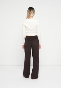 Krém színű, kábelmintás, cropped pulóver, sötétbarna, széles szárú nadrággal párosítva, hátsó zsebekkel. Simább textúrák, fitted derék és harangszárak.