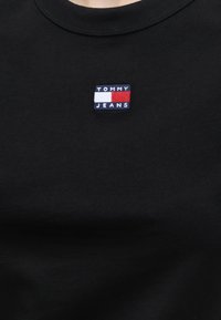 Μαύρο t-shirt με μικρό λογότυπο Tommy Jeans με χρώματα κόκκινο, λευκό και μπλε, τοποθετημένο κεντρικά κάτω από το λαιμόκοψη.