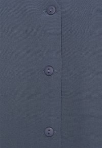 Chemise bleu marine à boutons avec un tissu texturé, comportant cinq boutons ronds et foncés le long de l'avant pour la fermeture.