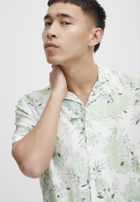 Camisa de manga corta en tejido ligero, con una base blanca y patrones florales verdes, además de un sutil diseño tropical.