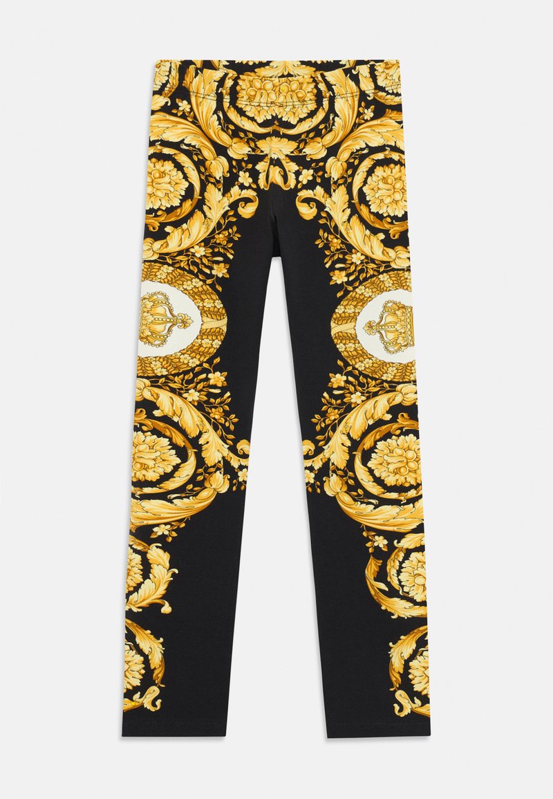Mustat legginsit, joissa on monimutkaisia kultaisia barokki-floraalikuvioita ja valkoisia mitalia, joissa on kultaisia kruunuja reisissä.