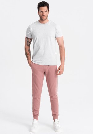 Hellgraues T-Shirt mit kurzen Ärmeln und einem Blättermuster, kombiniert mit weichen rosa Jogginghosen und weißen Sneakers. Einfaches und lässiges Design.