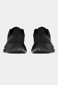 Must pärgade mustad jooksujalatsid, millel on täpilised tallad, vaadatuna tagant, lihtsal valgel taustal.