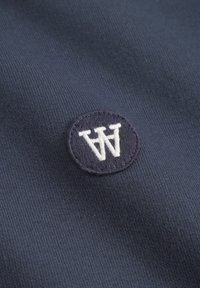 Navy blue fabric with a soft texture featuring a circular embroidered patch. The patch contains a white "W" and is bordered in dark blue.