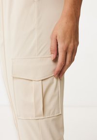 Beige cargobyxor med sidoficka. Tillverkade av ett mjukt tyg, med en veckad design och sydda detaljer.