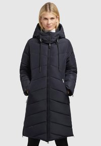 Găleată sau vestă de puf de culoare albastru marin, cu un siluet lung, cusături în zigzag, glugă ajustabilă și buzunare laterale, având o închidere cu fermoar în față.