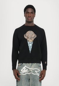 Zwarte sweatshirt met een grote afbeeldingen van een ijsje in beige en blauw. Kenmerkt zich door een ronde hals en geribbelde manchetten. Gedetailleerd met opvallende accenten op de broek.