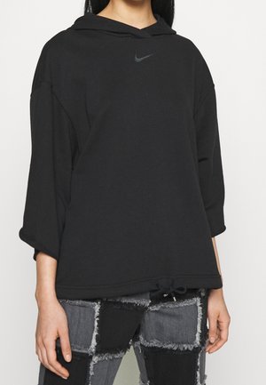 Kvinde iført en løs sort Nike hoodie med trekvartlange ærmer og patchwork sorte og grå frynsete jeans.