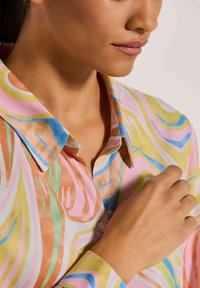 Mehrfarbiges Hemd mit einem fließenden, abstrakten Muster in Pink, Gelb, Blau und Grün. Verfügt über einen knöpfbaren Kragen und eine weiche Stoffstruktur.