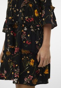 Svart volangklänning med ett blommönster i gult, rosa och vitt, med lager på lager och mjuk tygtextur.