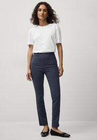 Pantaloni elasticizzati blu navy con una comoda cintura elastica, abbinati a una maglietta bianca a maniche corte e scarpe nere senza tacco, in piedi su uno sfondo neutro.