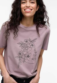 Lys lilla T-shirt med korte ærmer, der har en sort linjetegning af et ansigt prydet med blomster og blade. Glat tekstur, afslappet pasform.