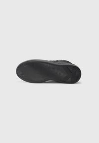 Fekete sneaker talp hullámzó mintázattal és márkás blokk sarokkal, fehér háttér előtt bemutatva.