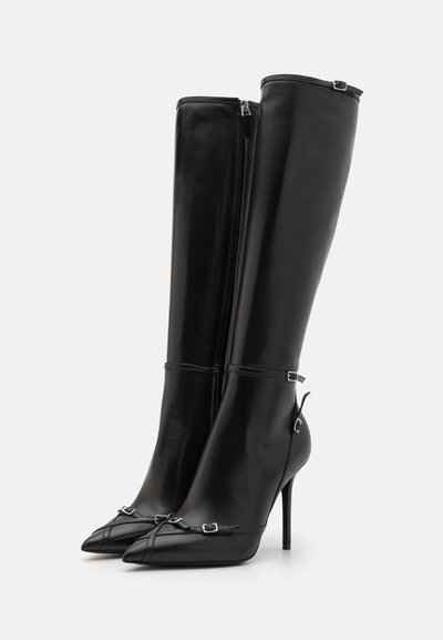 Botas de cuero negras hasta la rodilla con puntas afiladas, tacones de aguja y acentos decorativos de hardware plateado. Textura suave con cierre de cremallera.