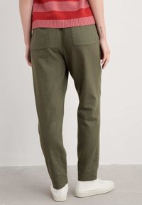 Olivegröna, lätta byxor med avslappnad passform, som har två bakfickor och uppknycklade anklar, i kombination med vita sneakers i låg topp.