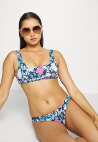 Conjunto de bikini floral com fundo azul-marinho e flores cor-de-rosa e brancas; inclui alças grossas e parte de baixo de cintura baixa combinando.