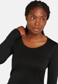 Camiseta negra de manga larga con cuello redondo, un diseño ajustado y una sutil textura acanalada. Las mangas llegan hasta las muñecas.