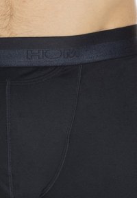 Närbild av en persons midja som bär svarta åtsittande kalsonger med en mörk midja som har subtilt präglad branding.