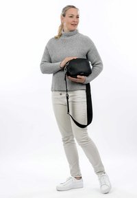 Borsa a tracolla in pelle nera con finitura texturizzata, hardware in argento e tracolla removibile, tenuta da una persona che indossa un maglione grigio.